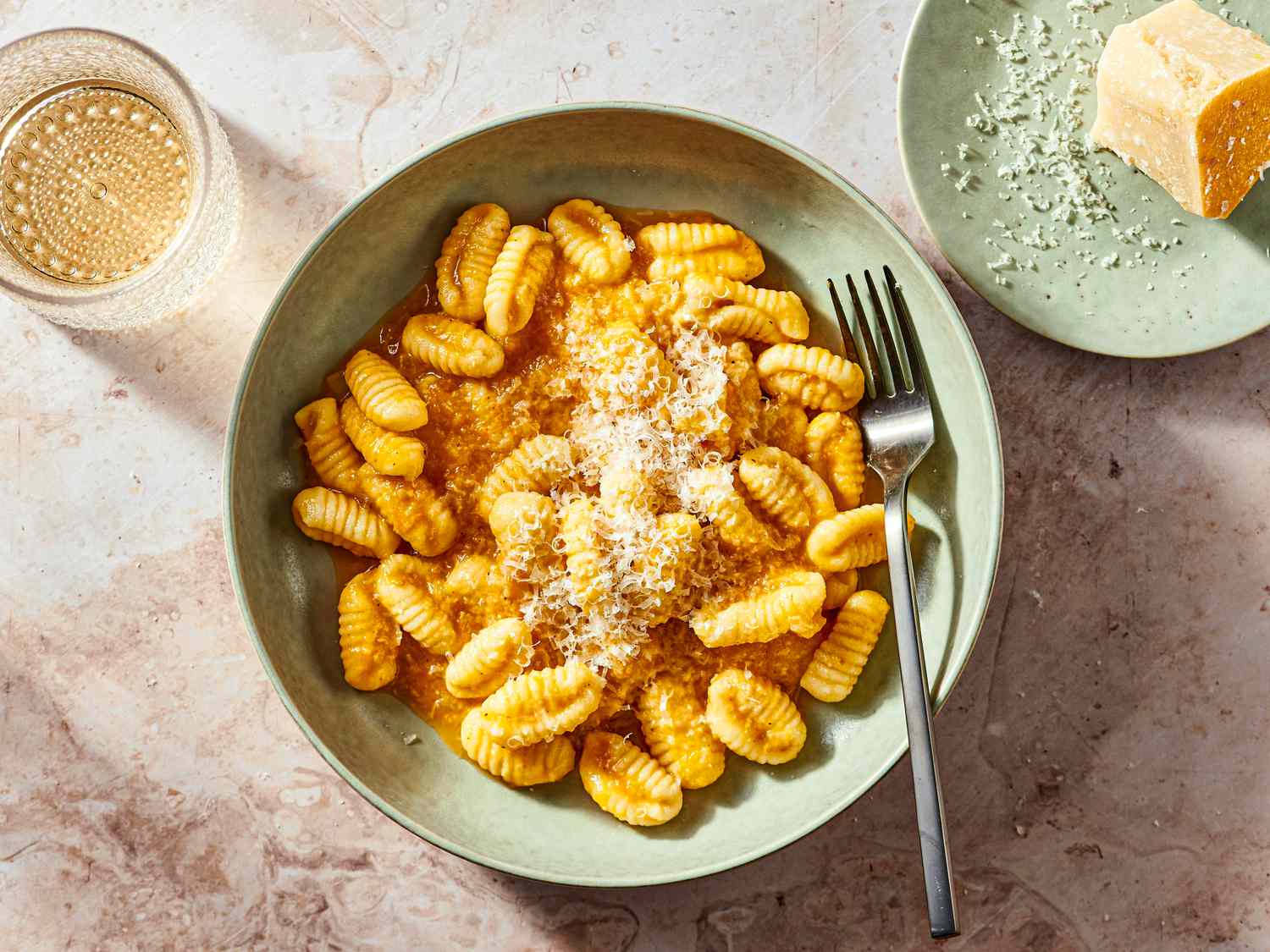 Fresh Cavatelli on a green bowl with a fork, with parmesan on a smaller green dish to the side, and a drink in a textured glass