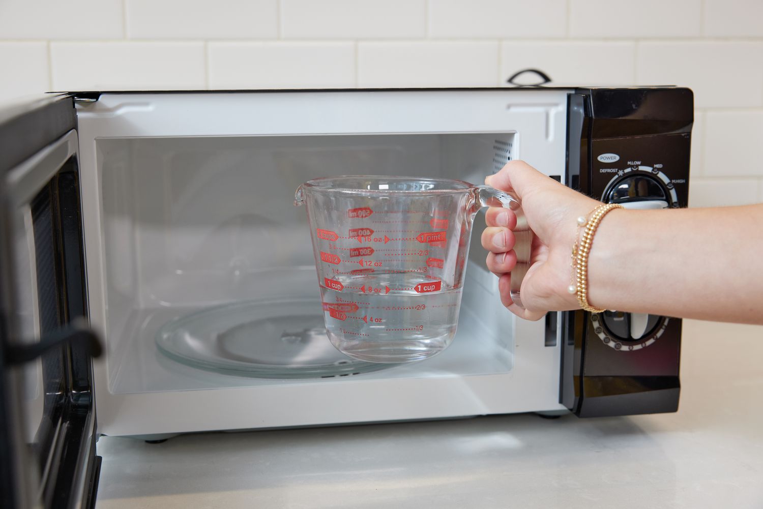 hand putting water in a measuring glass into the microwave