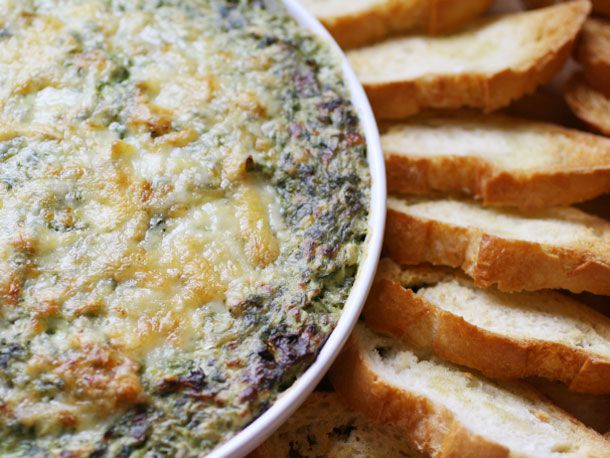 Closeup of a bowl of Boursin and Gruyère spinach artichoke dip flanked with slices of toasted baguette.