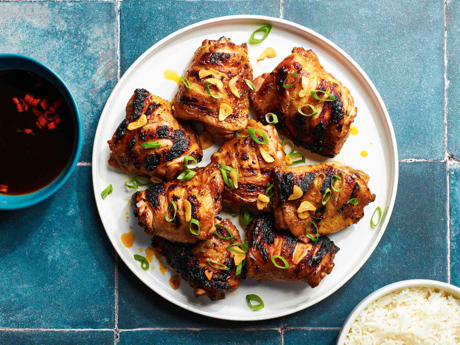 Chicken Inasal on a white plate next to dipping sauce and a bowl of white rice