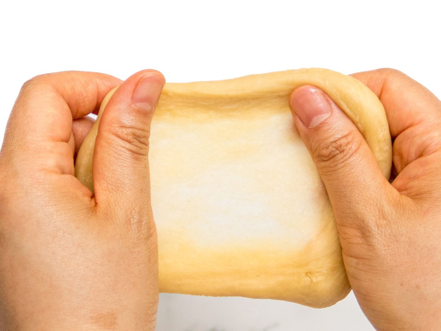 Hands holding up dough, checking the consistency using the window pan test 