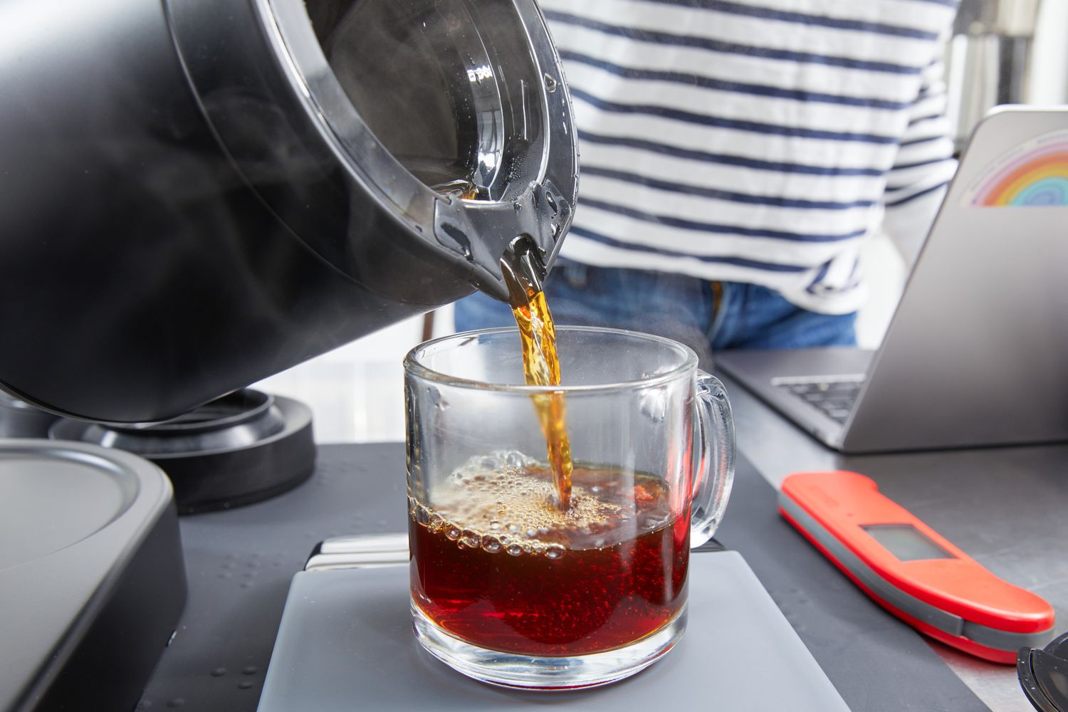 A person pouring coffee from the Ratio Six Coffee Maker's carafe into a mug.