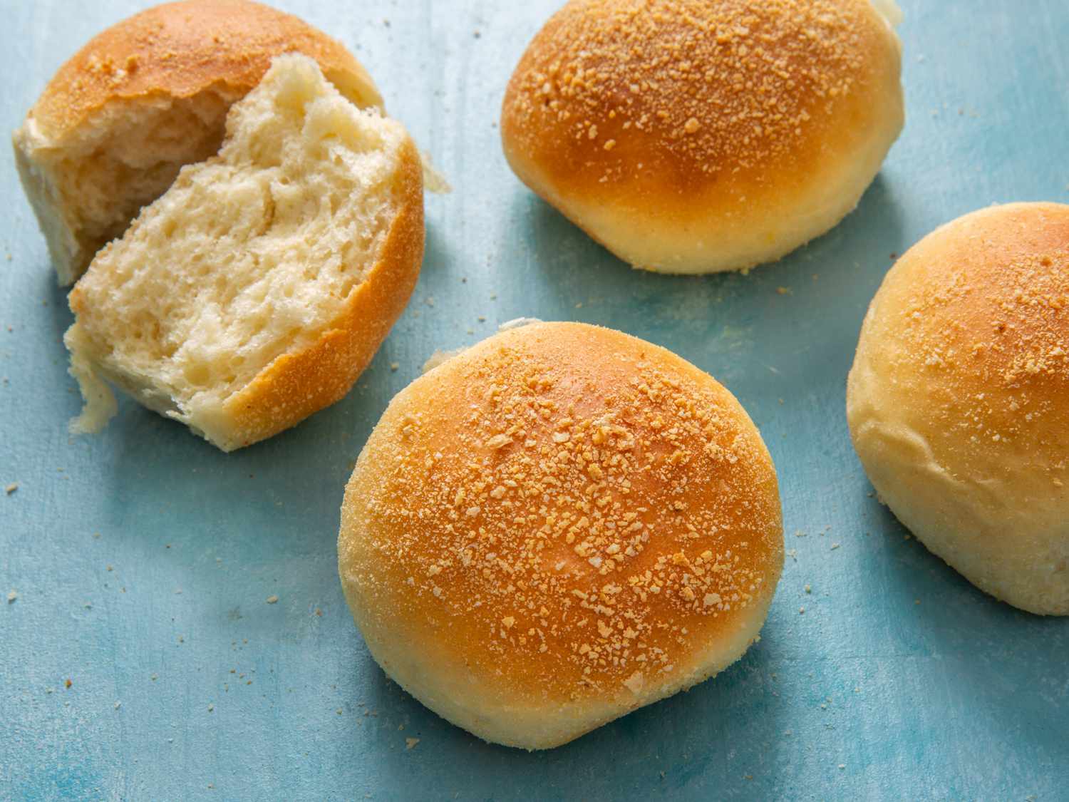 a few pandesal on a light blue background, one in the back split open to see inside