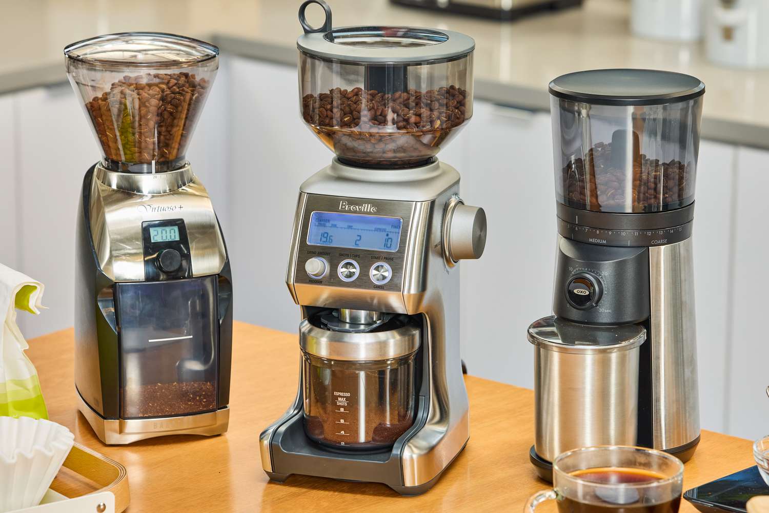 Three burr coffee grinders on a kitchen countertop.