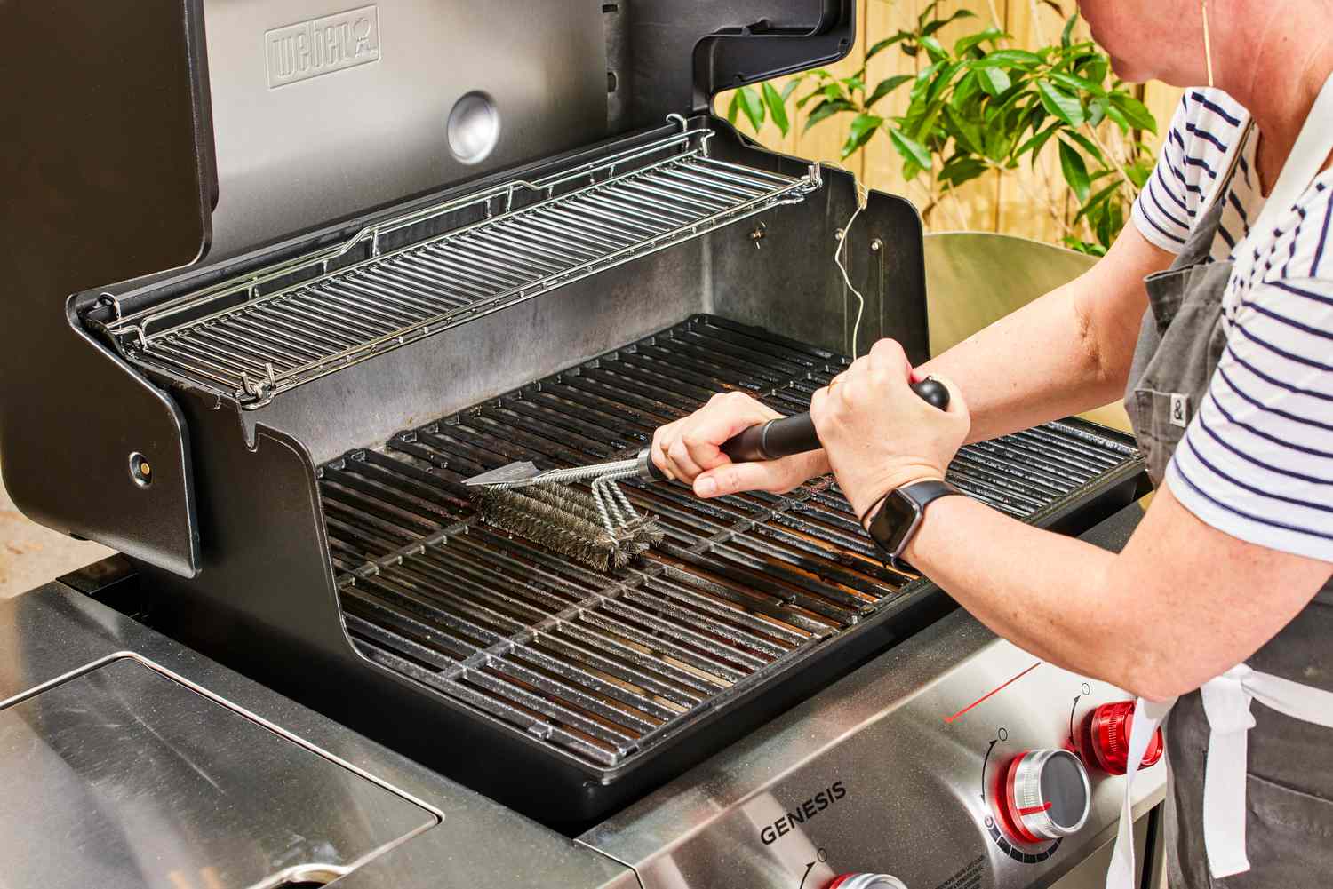 A person uses a grill brush to clean the Weber Genesis E-335 Gas Grill