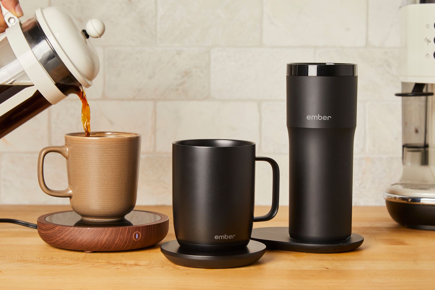 French press coffee is poured into a coffee mug on a warming pad, surrounded by two temperature control mugs