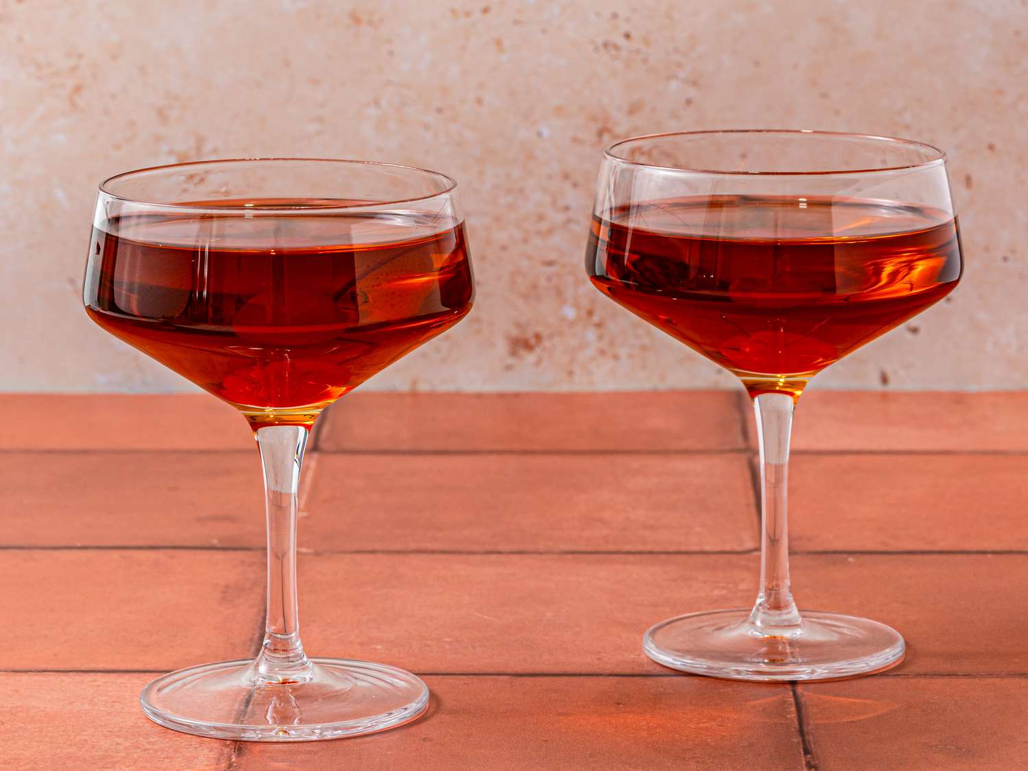 Two Manhattans in stemmed cocktail glasses on a wooden surface