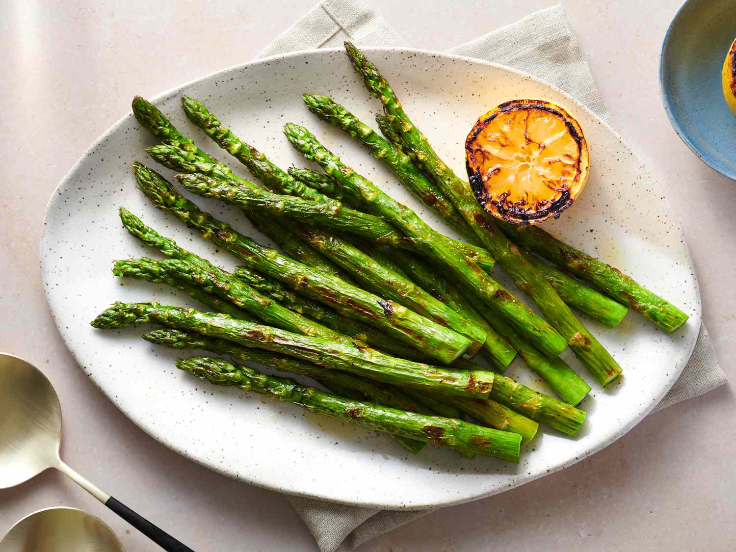 Grilled asparagus served on a large serving plate, drizzled with olive oil, with lemon squeezed over the top, and garnished with charred lemons.