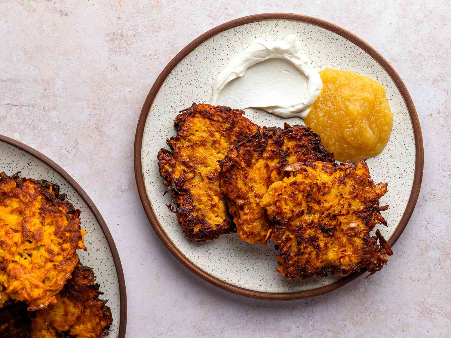 Three crispy sweet potato latkes on a ceramic plate alongside apple sauce and sour cream.