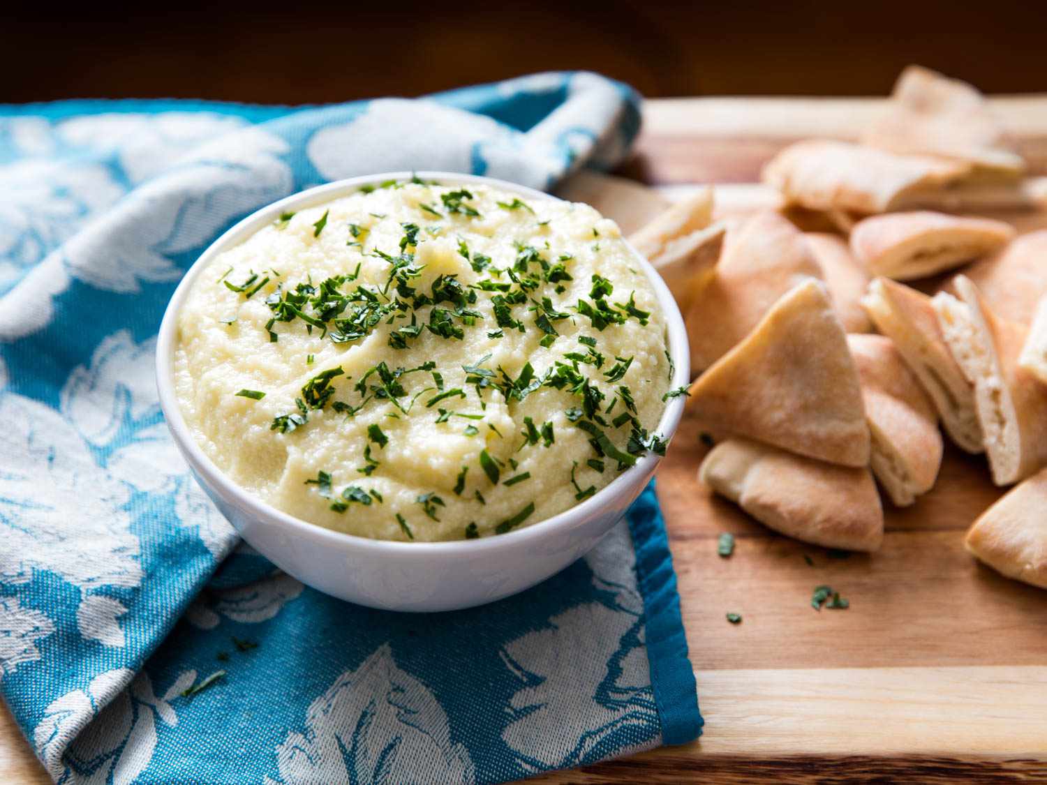 Bowl of puree potato topped with fresh herbs next to a pile of sliced pita bread