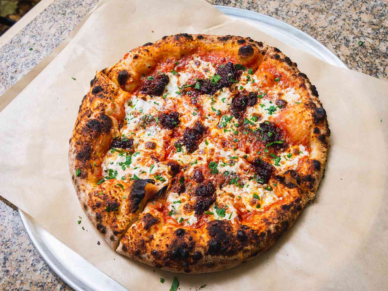 Nduja pizza cooked in outdoor pizza oven on a piece of parchment set on a pizza pan