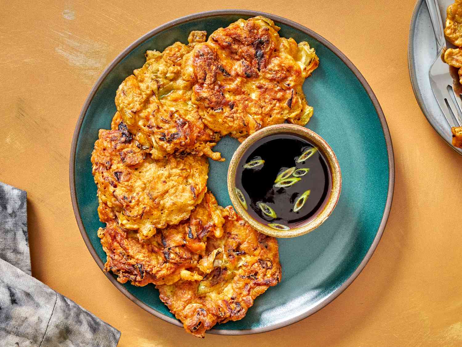 Vegetable pancakes on a blue plate with dipping sauce sprinkled with scallions.