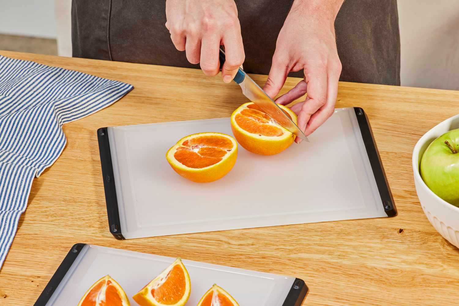 A person slicing an orange on the OXO plastic cutting board.