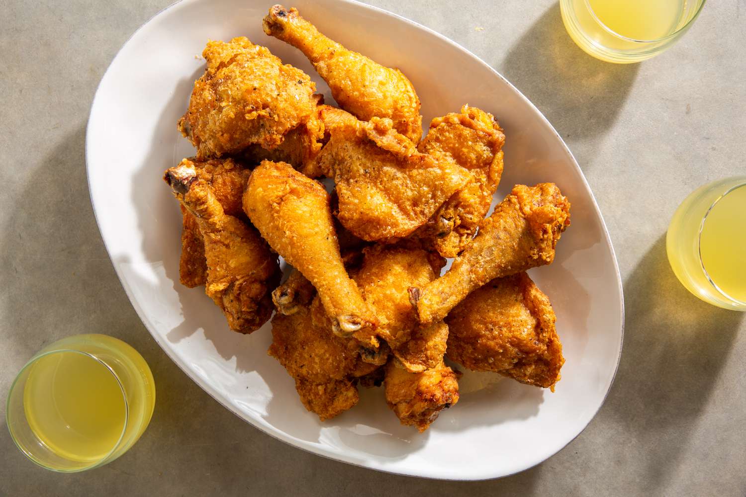 Platter of batter-fried chicken pieces flanked by yellow drinks on marble surface