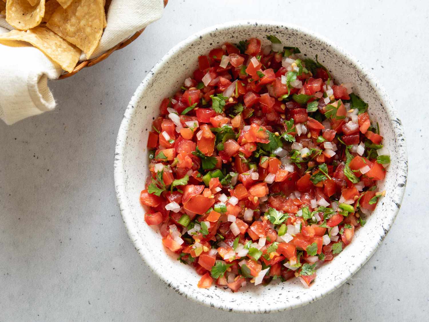 A bowl of pico de gallo with tortilla chips on the side