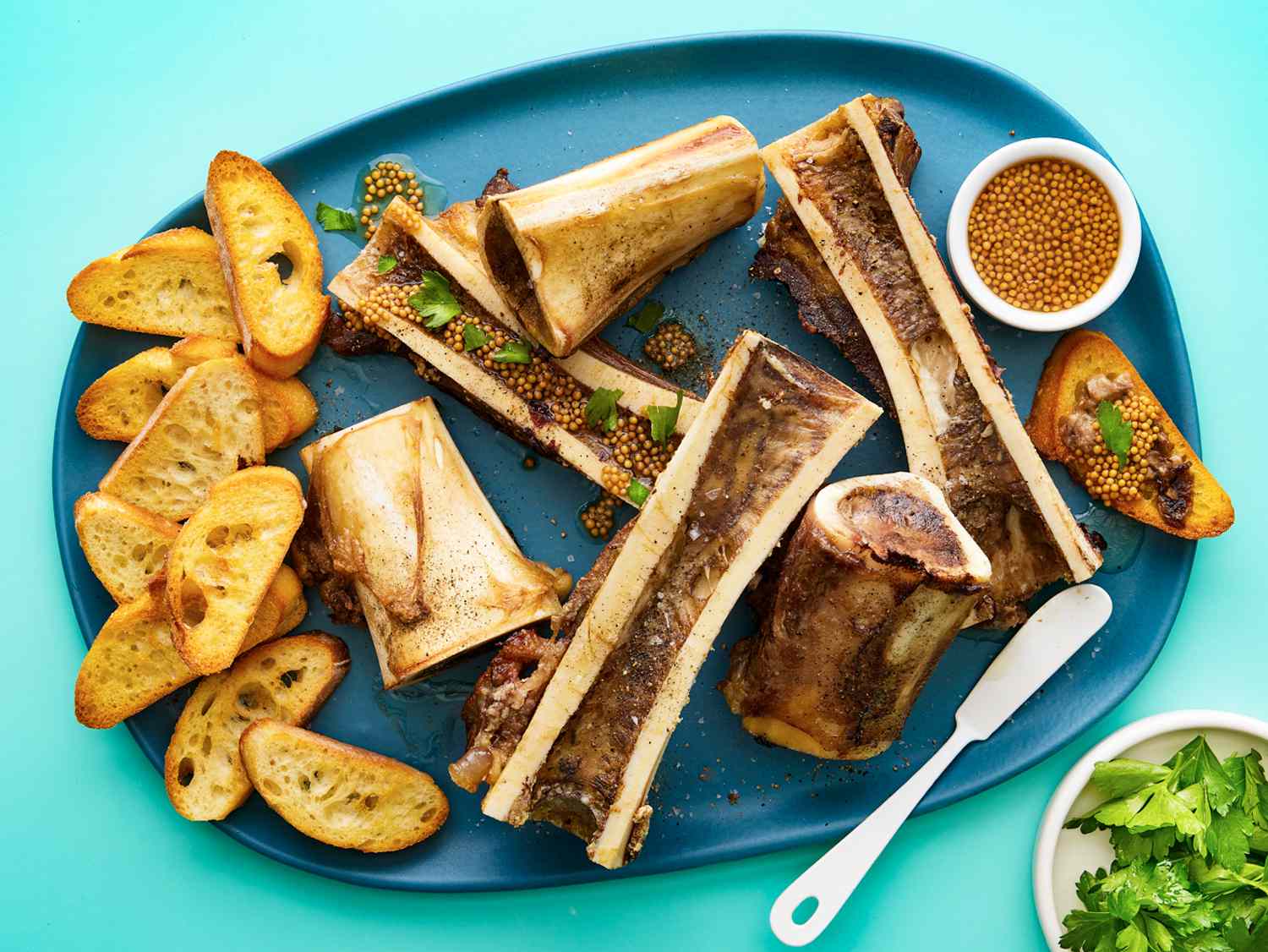 Overhead view of roasted bone marrow on a plate with toasted baguettes mustard and parsely 