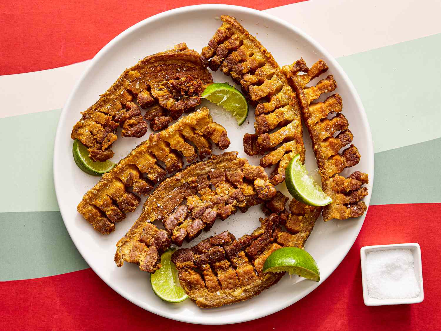 Overhead view of chicharrones on a plate with a small bowl of salt off to the side. 