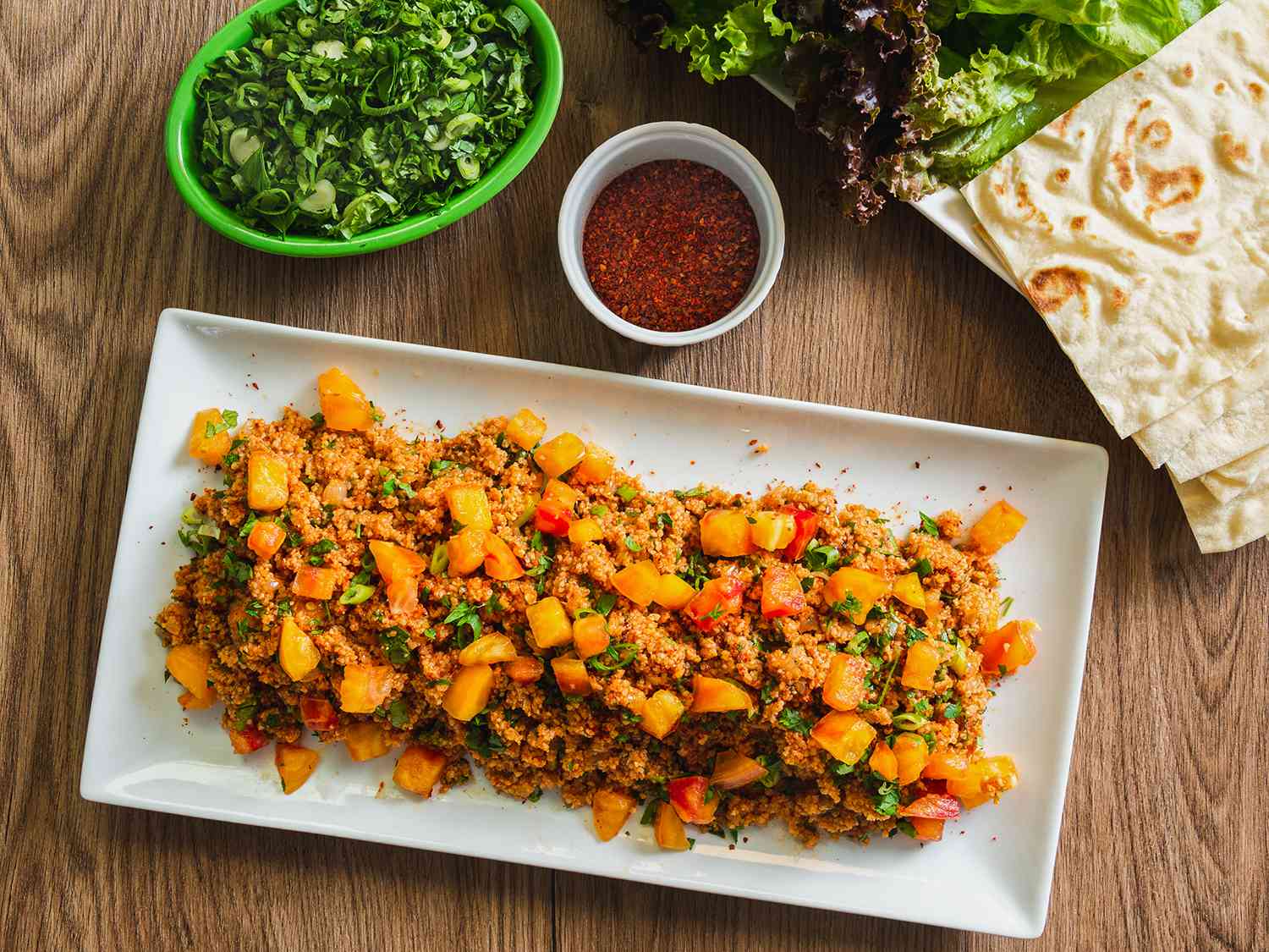 Platter of eetch served with herb salad, lettuces, and lavash.