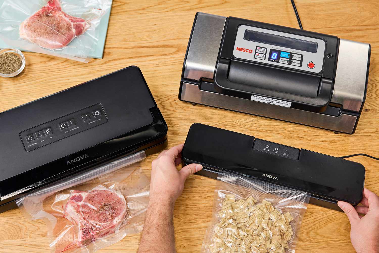 Three vacuum sealers on a kitchen countertop. Once is being used to vacuum seal a pork chop and another cereal.