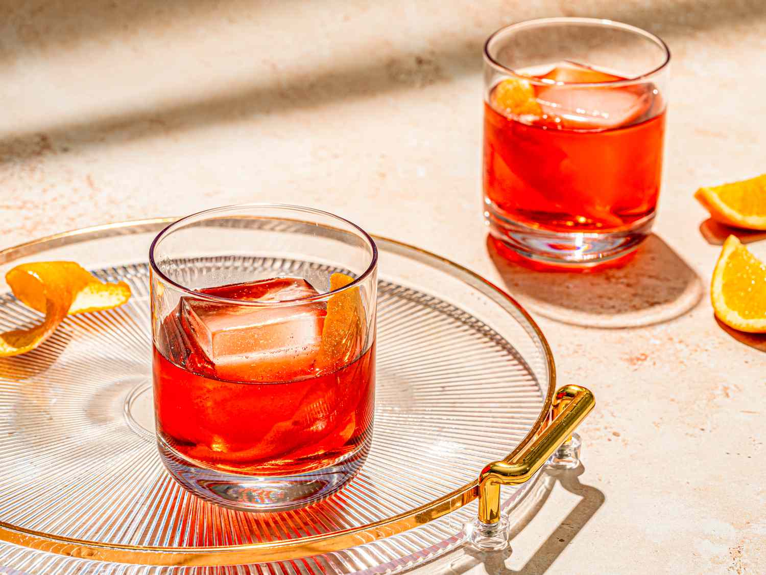 Two Negroni cocktails served in old-fashioned glasses with orange peels, with one served on a glass tray