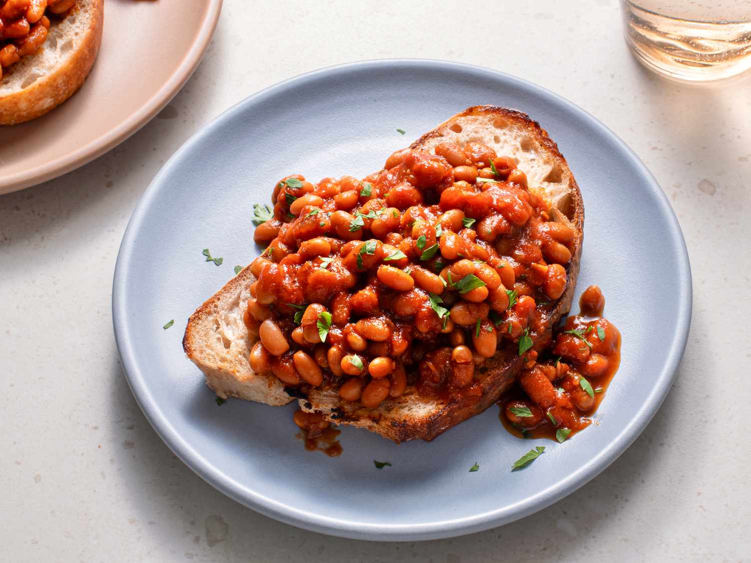 British-style baked beans on a piece of white bread which is placed on a blue ceramic plate on a stone background.