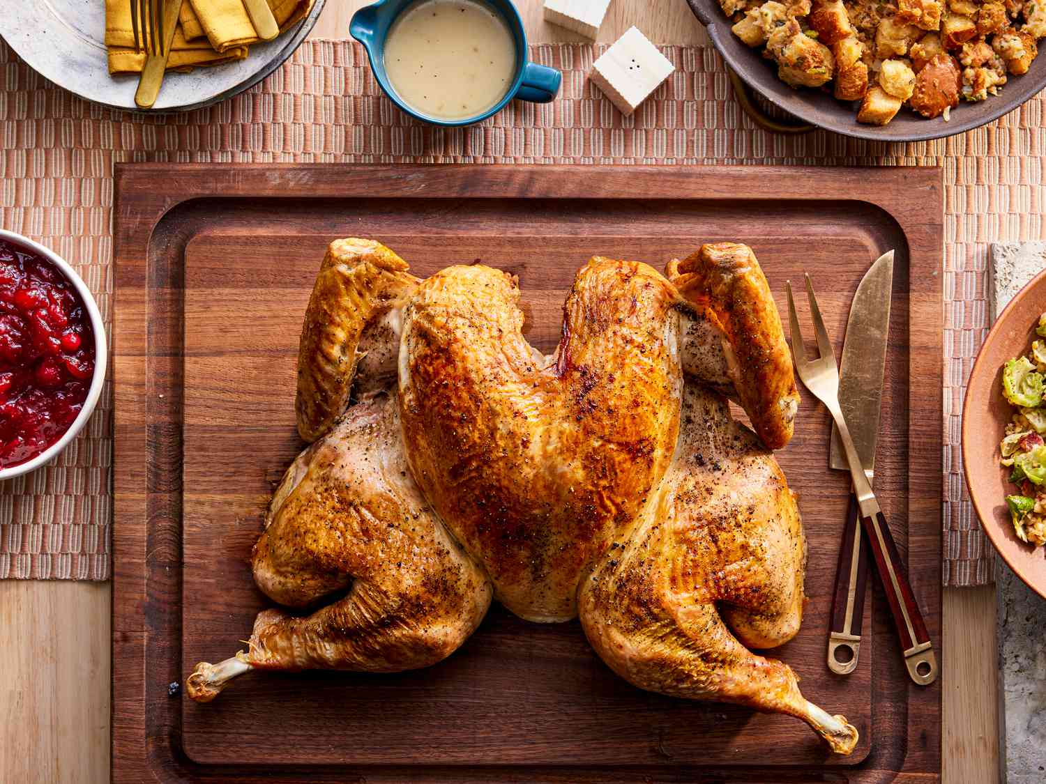 Spatchcocked Turkey on a wooden carving board surrounded by Thanksgiving dishes