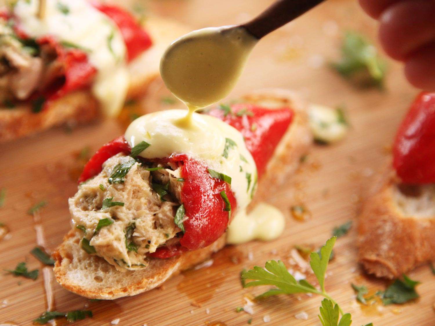 A close-up of pimientos del piquillo rellenos de atún (Spanish tuna-stuffed piquillo peppers) with sauce being drizzled with a spoon.