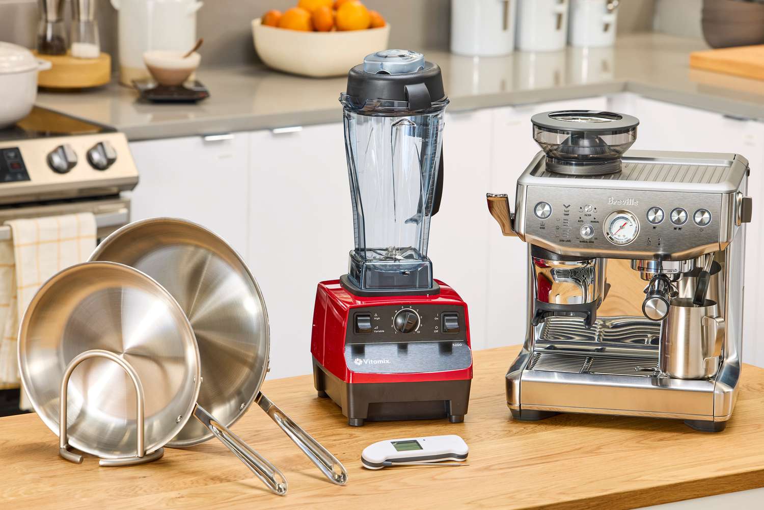 An espresso machine, stainless steel skillets, instant-read thermometer and blender on a kitchen countertop.