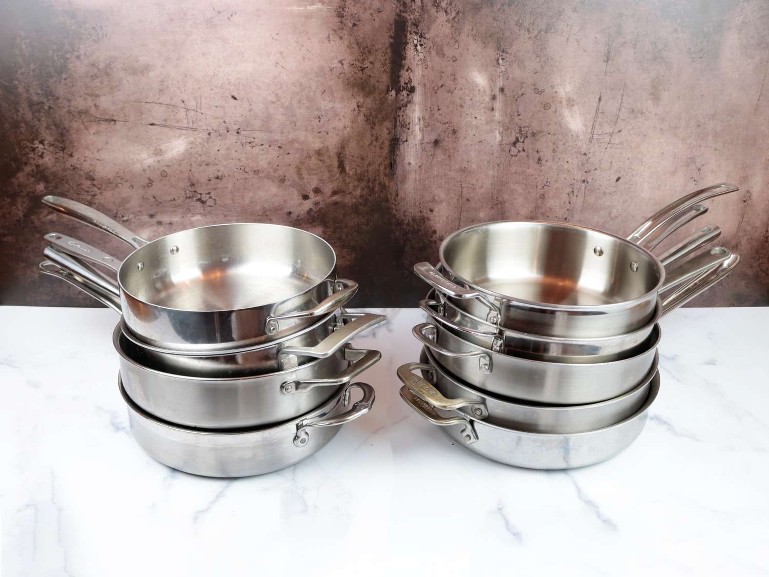 nine different saute pans on a marble counter in two stacks