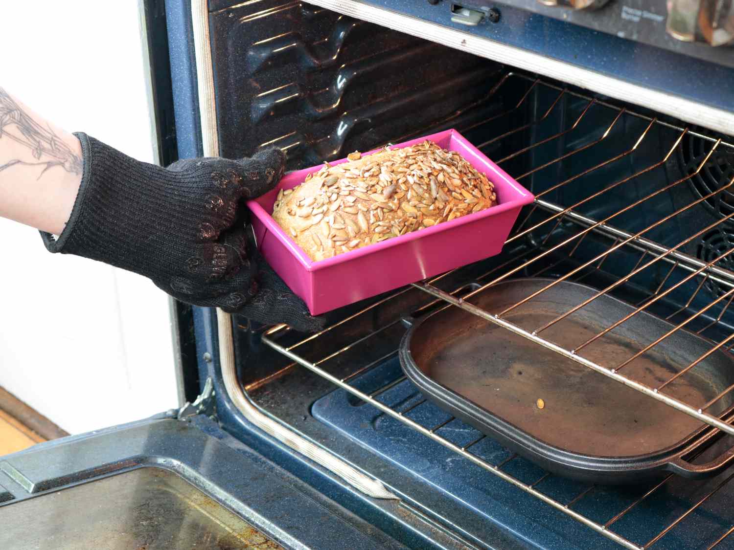 a hand taking a loaf of bread out of the oven in a pink loaf pan