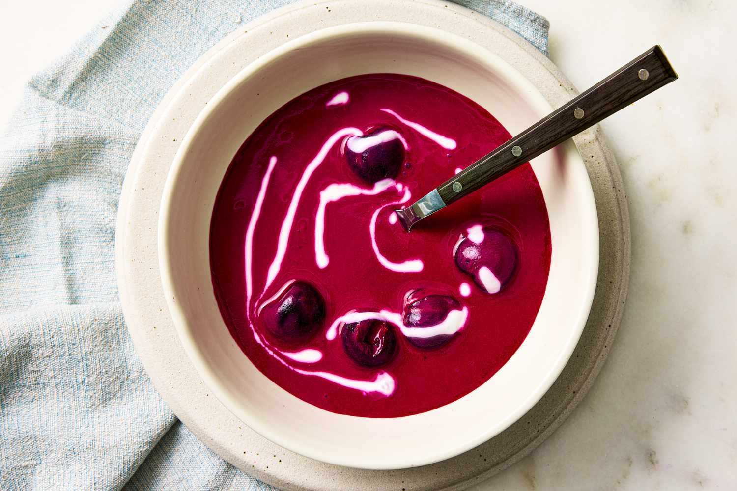 A bowl of beet and cherry soup with a swirl of sour cream