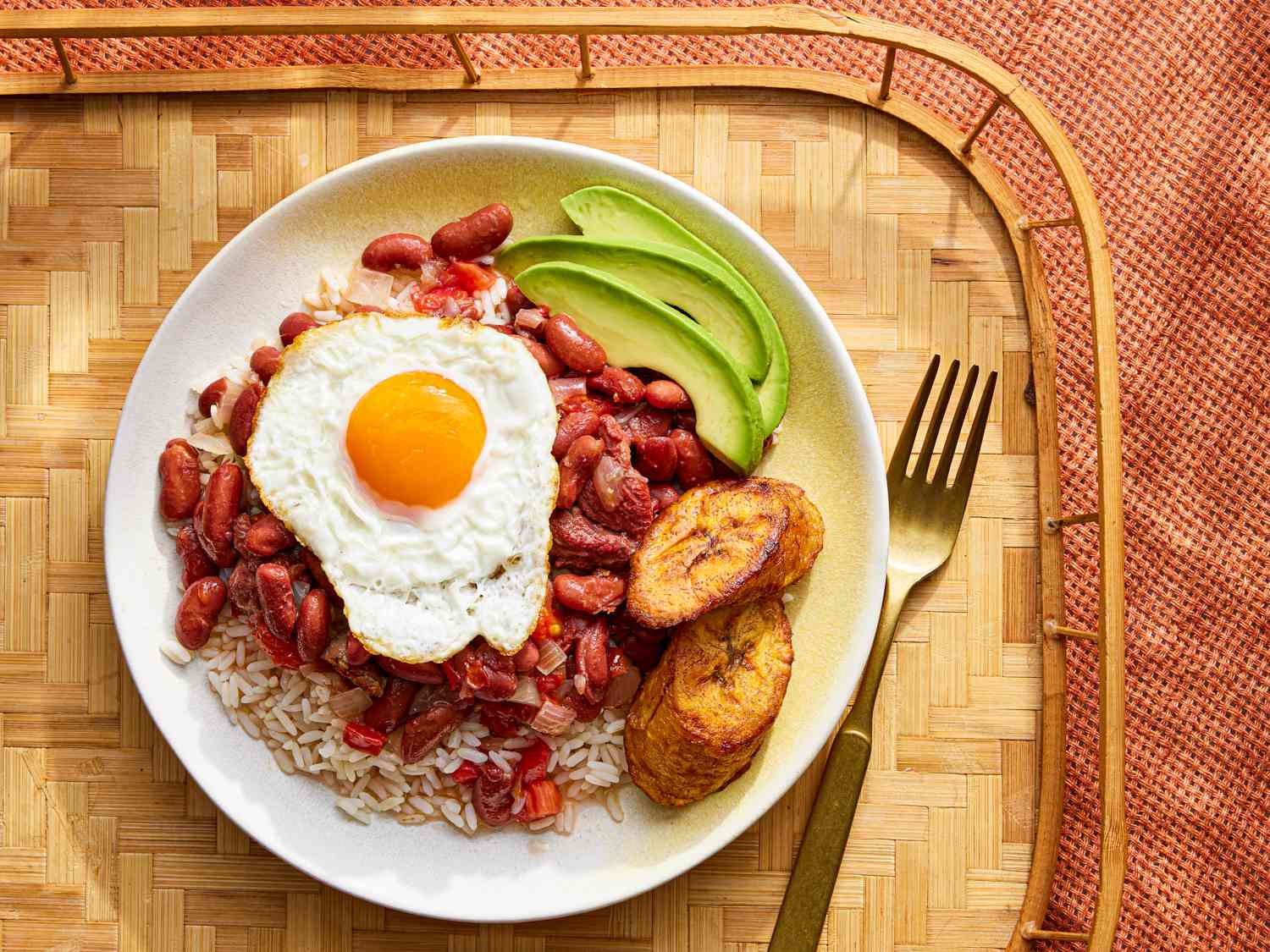 Overhead view of Colombian beans and rice on a plate and a wooden tray with a fried eggs