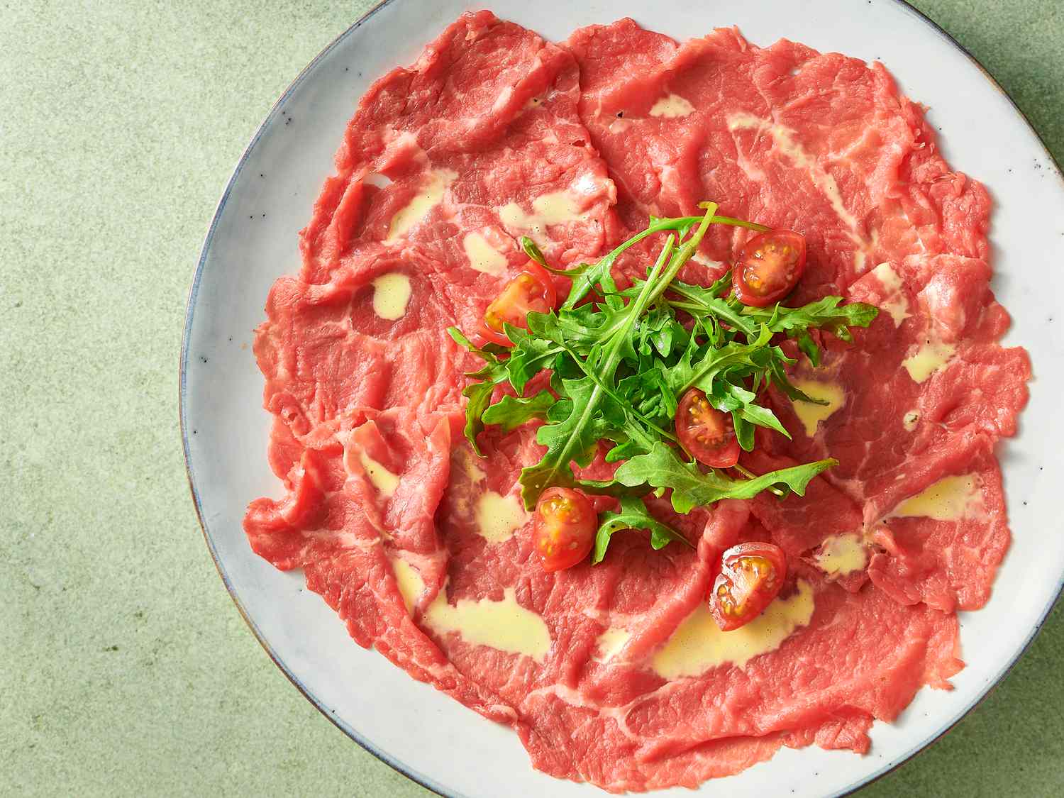 beef carpaccio garnished with tomato quarters and baby arugula