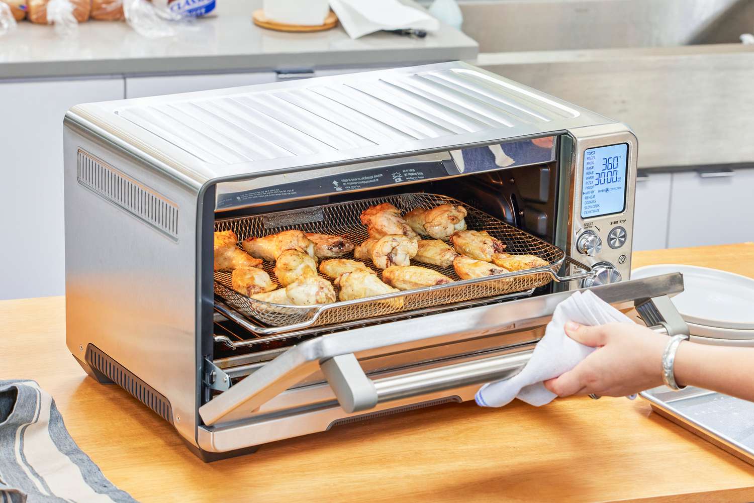 A hand opening the door to chicken cooking in the Breville the Smart Oven Air Fryer