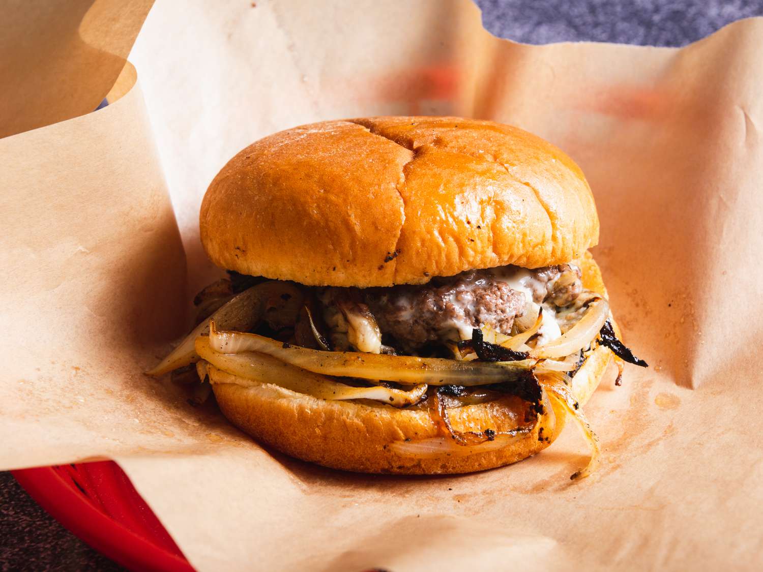 An Oklahoma style onion burger on deli paper in a red plastic deli basket. 