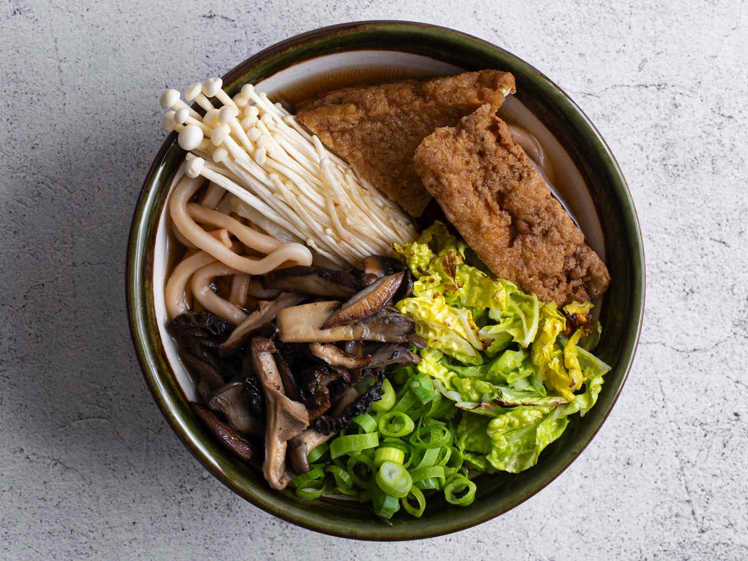 Japanese udon noodles in a ceramic bowl with mushroom-soy broth, stir-fried mushrooms, raw mushrooms, sliced scallions, cabbage, and tofu.