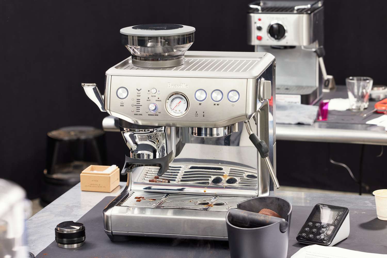 A Breville espresso machine on a countertop, with a knockbox and a tamper beside it.