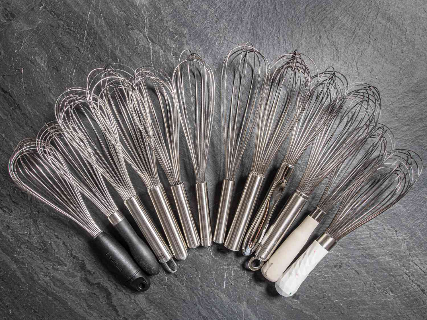 12 ballon whisks laid out in a semi circle on a piece of grey slate