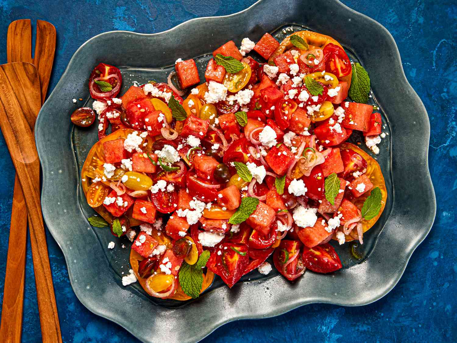 A dark bowl with tomato-watermelon salad, sprinkled with mint and feta, 