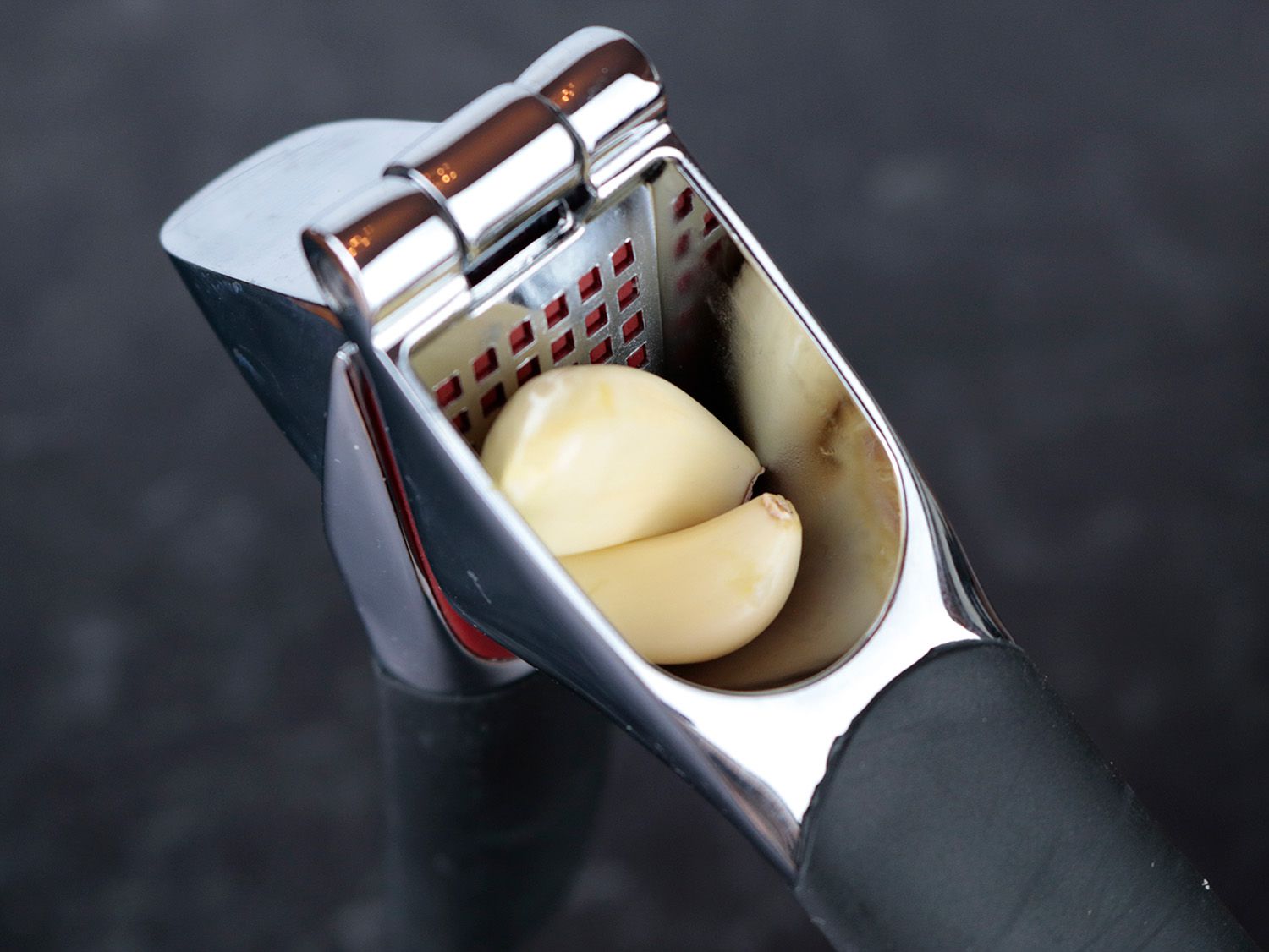 the hopper of a garlic press with two cloves inside of it