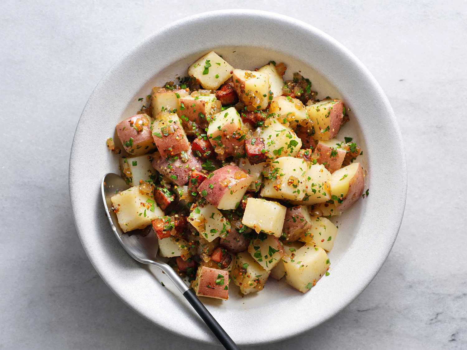 German potato salad in a white ceramic bowl with a spoon.