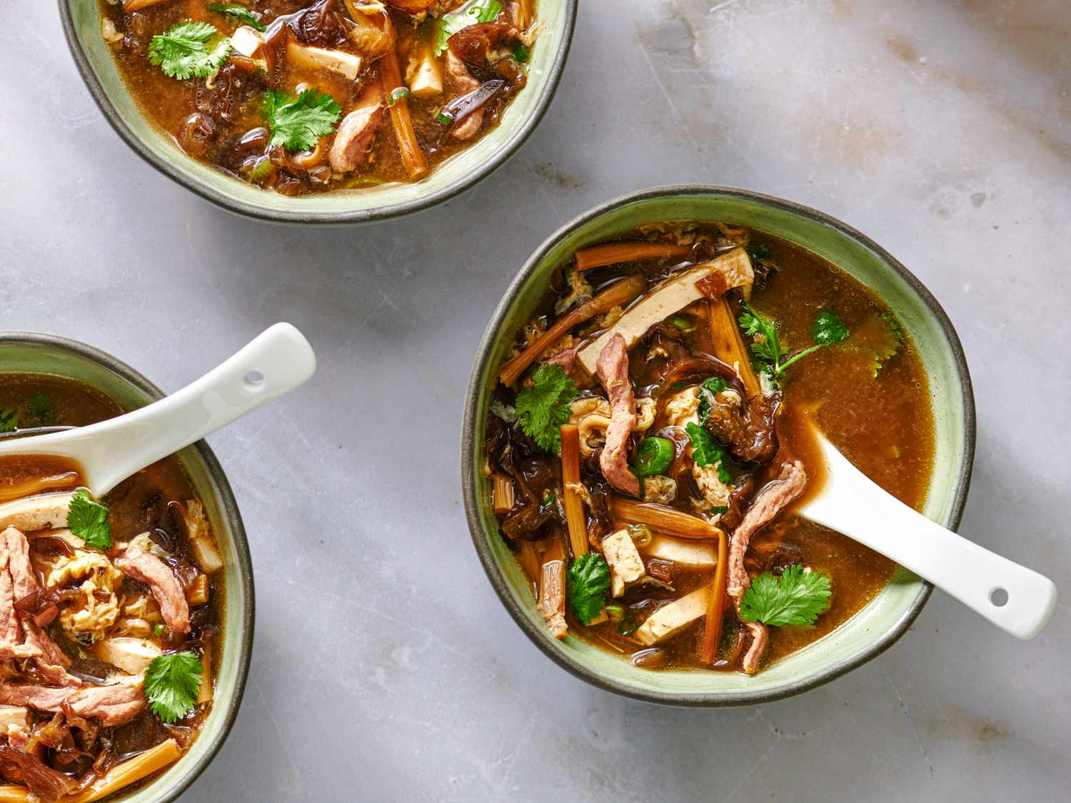 Three bowls of hot and sour soup, each with a ceramic soup spoon in it.