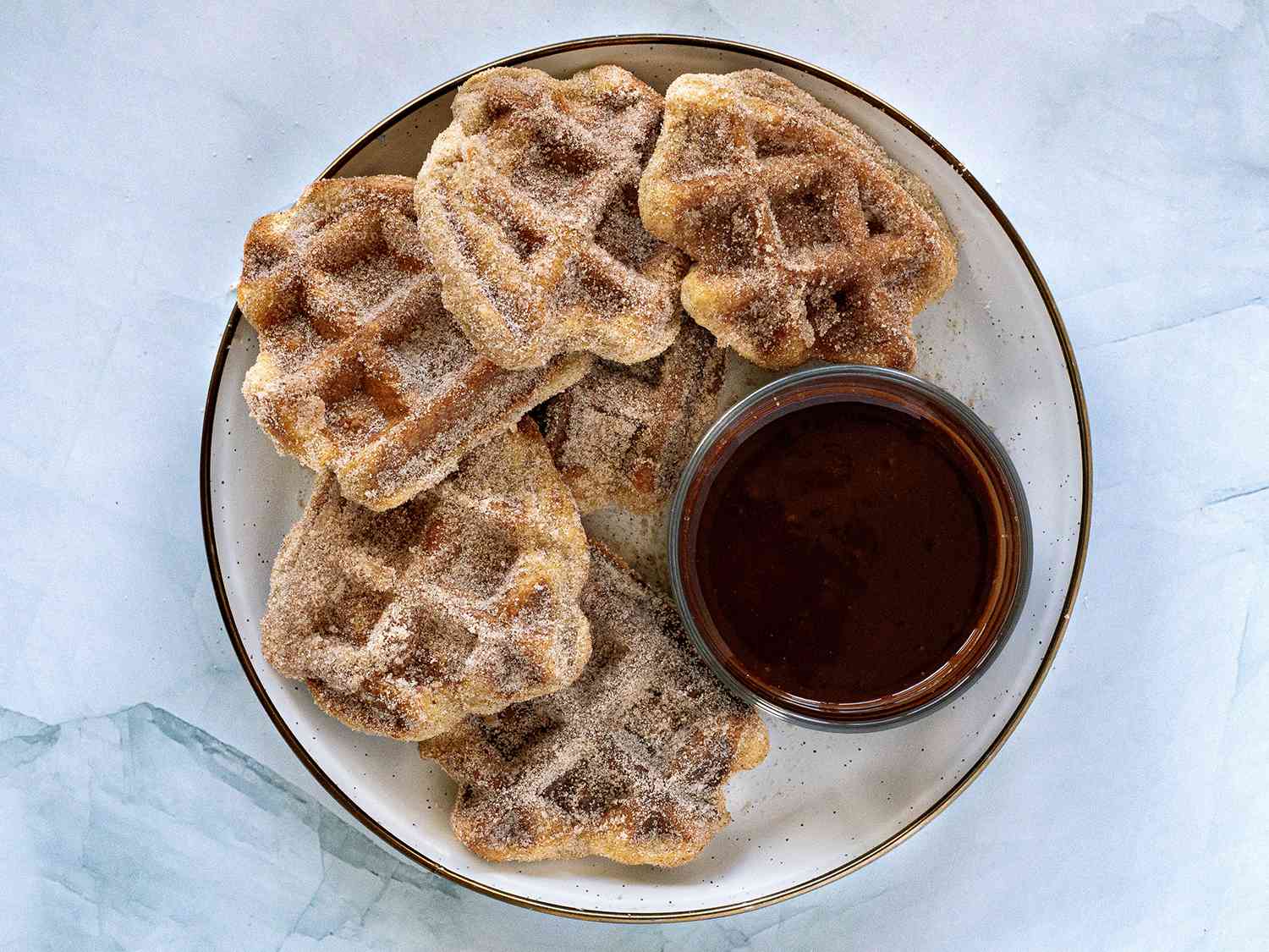 Waffle iron churros with dipping sauce on a plate, on a stone surface.