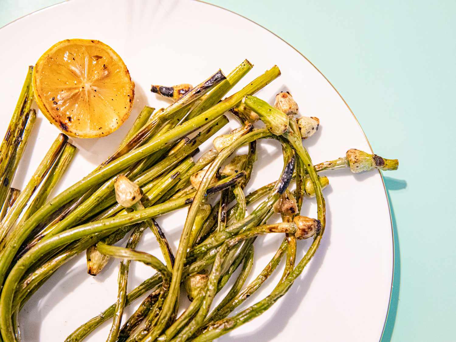 Grilled Garlic scapes on a white plate with a lemon 