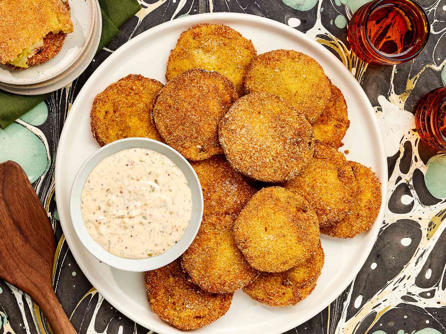 Overhead of Fried Green Tomatoes and dip on a printed surface. Plate on the corner has bitten tomatoes on it