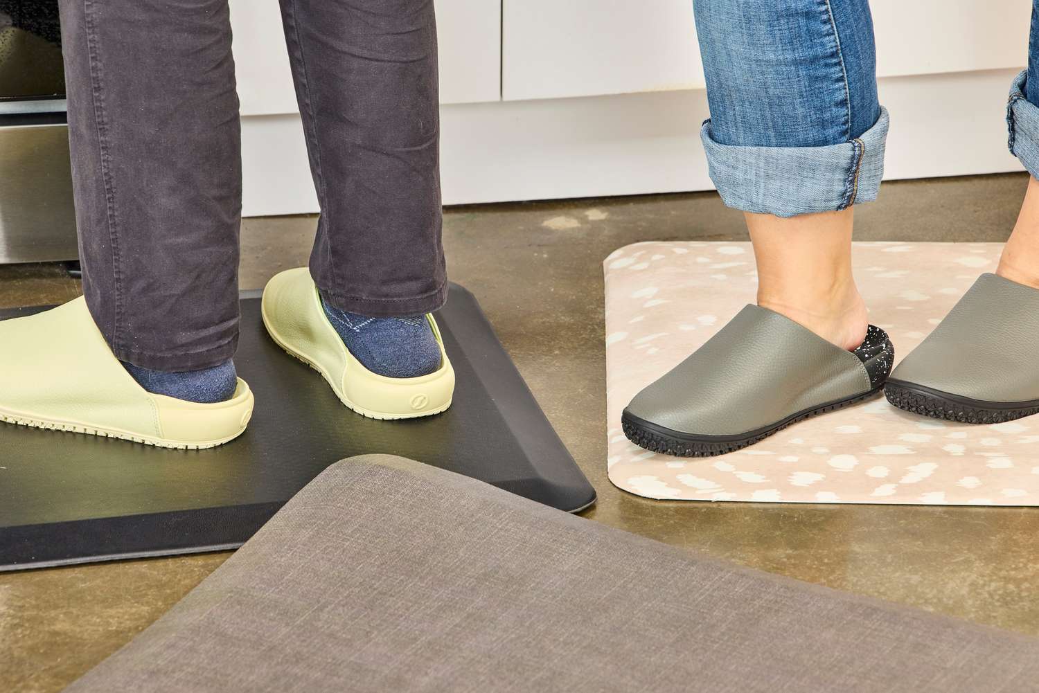 A closeup of two people's feet in kitchen clogs standing on anti-fatigue mats