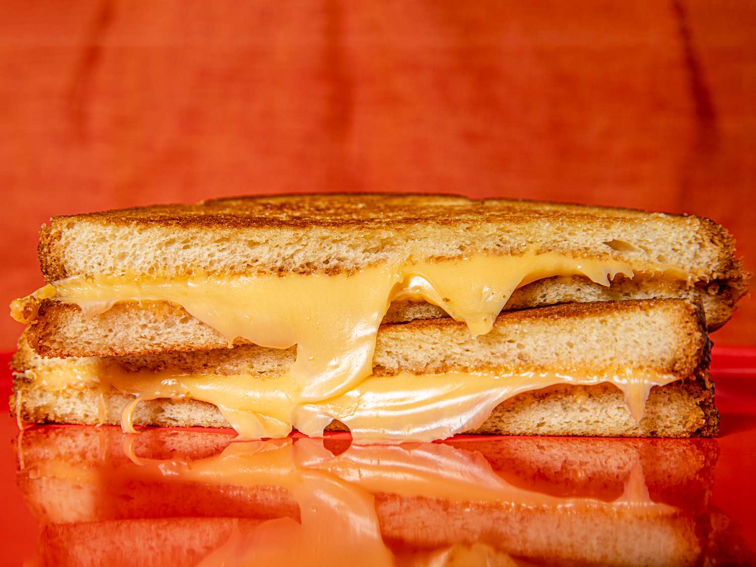 Two halfs of a grilled cheese stacked on top of each other with cheese dripping down the front.