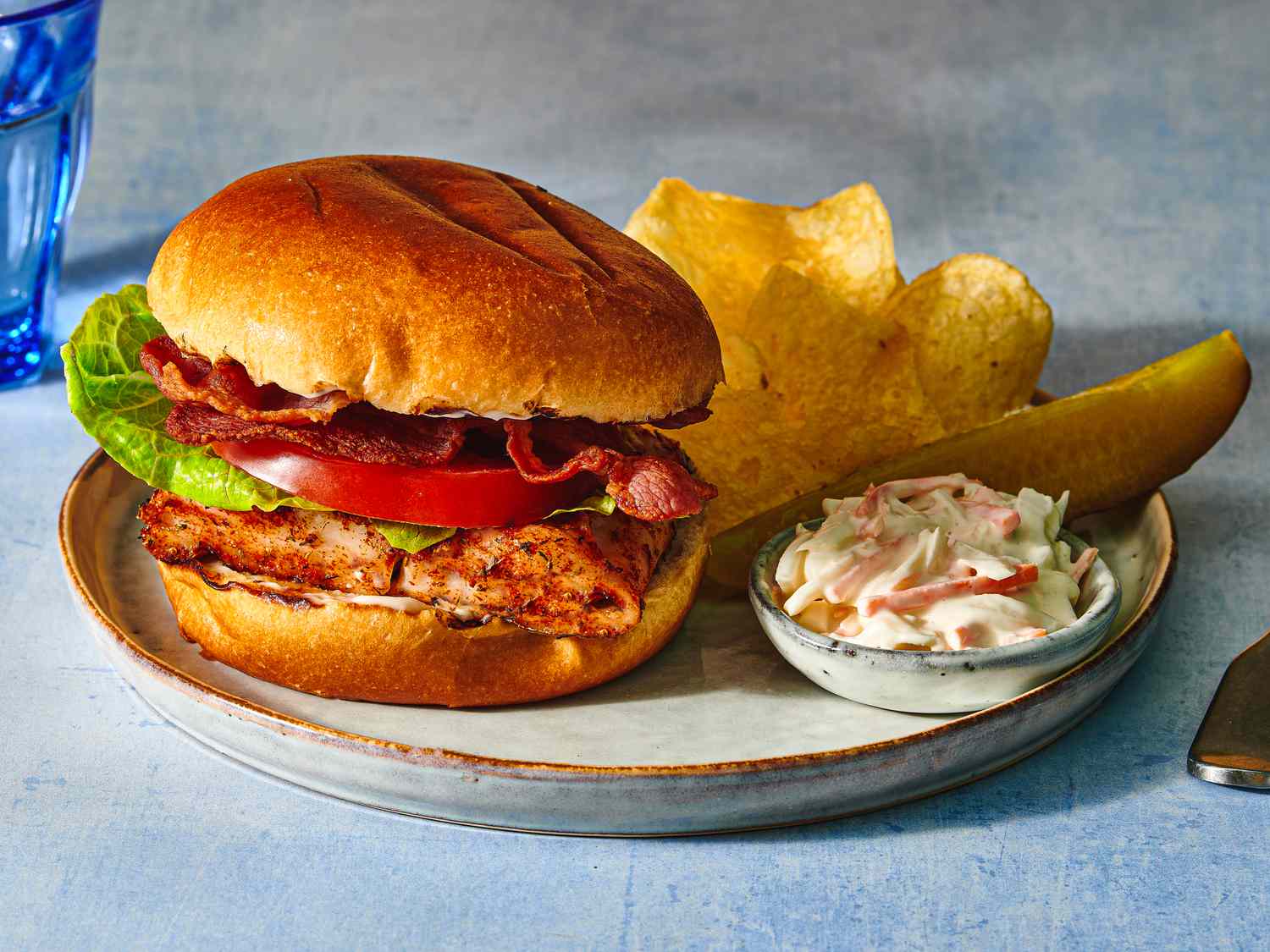 Grilled blackened-fish sandwich on a plate with potato chips, creamy coleslaw, and a pickle spear