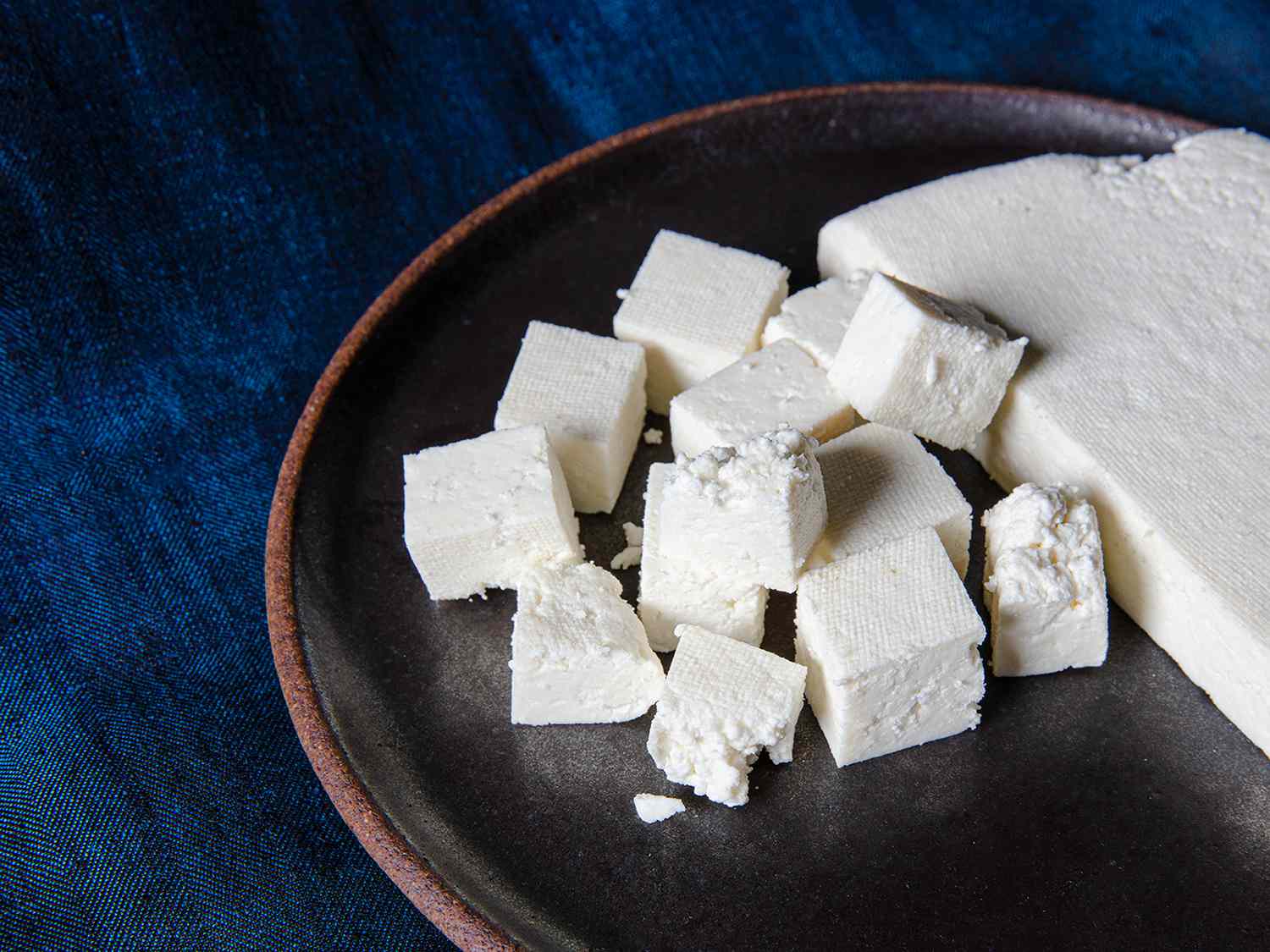 Fresh paneer on a brown plate on a blue backdrop