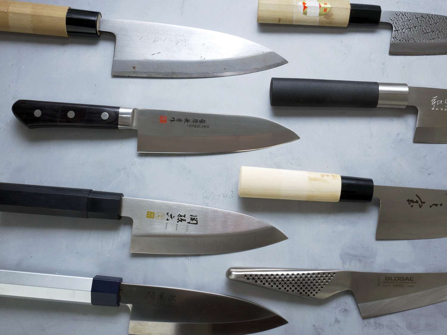 a variety of deba knives on a pale grey concrete surface